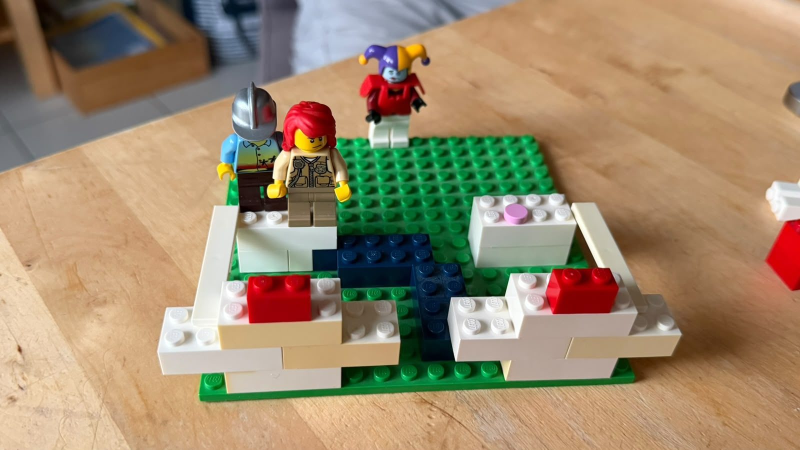 12 von 12 August 2026: selbst gebautes LEGO® Modell auf grüner Grundplatte, weiße und beige Mauern, ein dunkelblauer Weg und drei Figuren