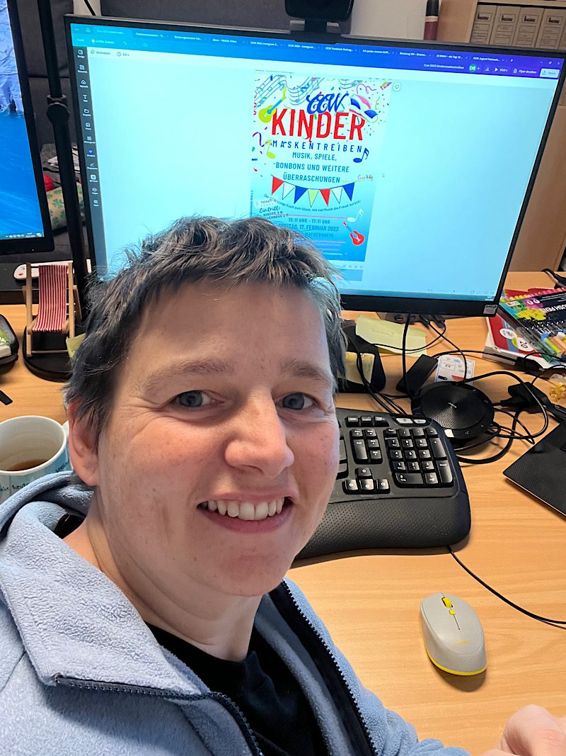 Danielle Berg am Schreibtisch, auf dem Bildschirm das Plakat für das CCW Kindermaskentreiben