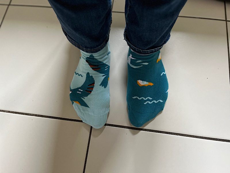 Füße in blaugrünen Socken mit Vogelmuster auf hellem Fliesenboden