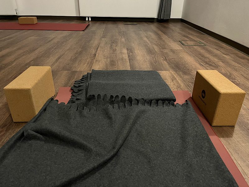 Vorbereiteter Yogaplatz: Decke auf einer roten Matte, links und rechts je ein Korkblock