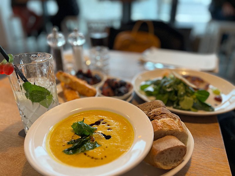 Gedeckter Restauranttisch mit Kürbissuppe, Baguette, Salat und einem Glas mit Minze