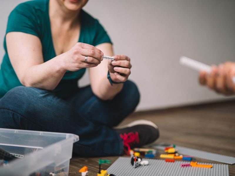 Hände halten einen kleinen beschrifteten Papierstreifen über einer Kiste mit LEGO-Steinen – Gefühle aufschreiben statt aussprechen.