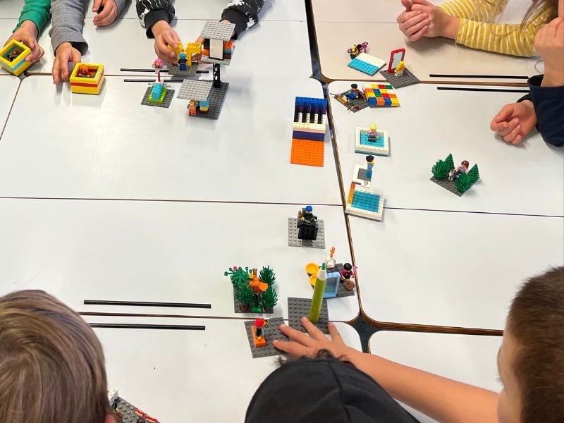 Kinderhände bauen bunte LEGO-Modelle an einem Tisch – LEGO® SERIOUS PLAY® Workshop „klasse Klasse!“ in einer Schulklasse.