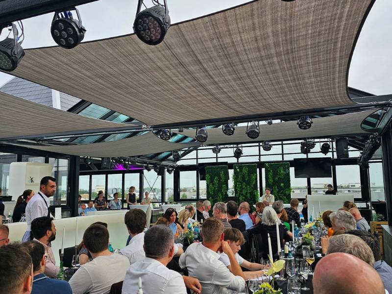 Menschen sitzen an Essenstafeln und hören einer Rede zu