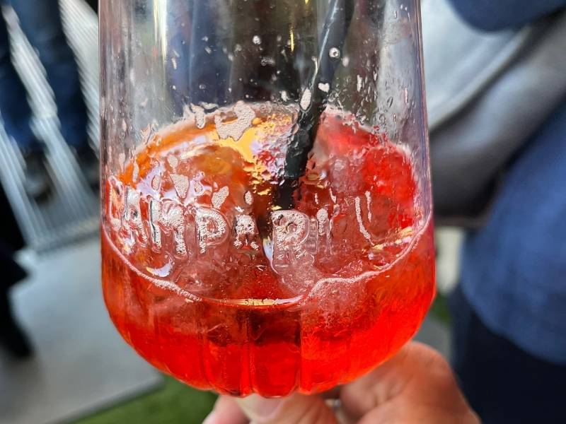 Glas mit Aufschrift Campari, halb gefüllt mit Campari Spritz und Strohhalm