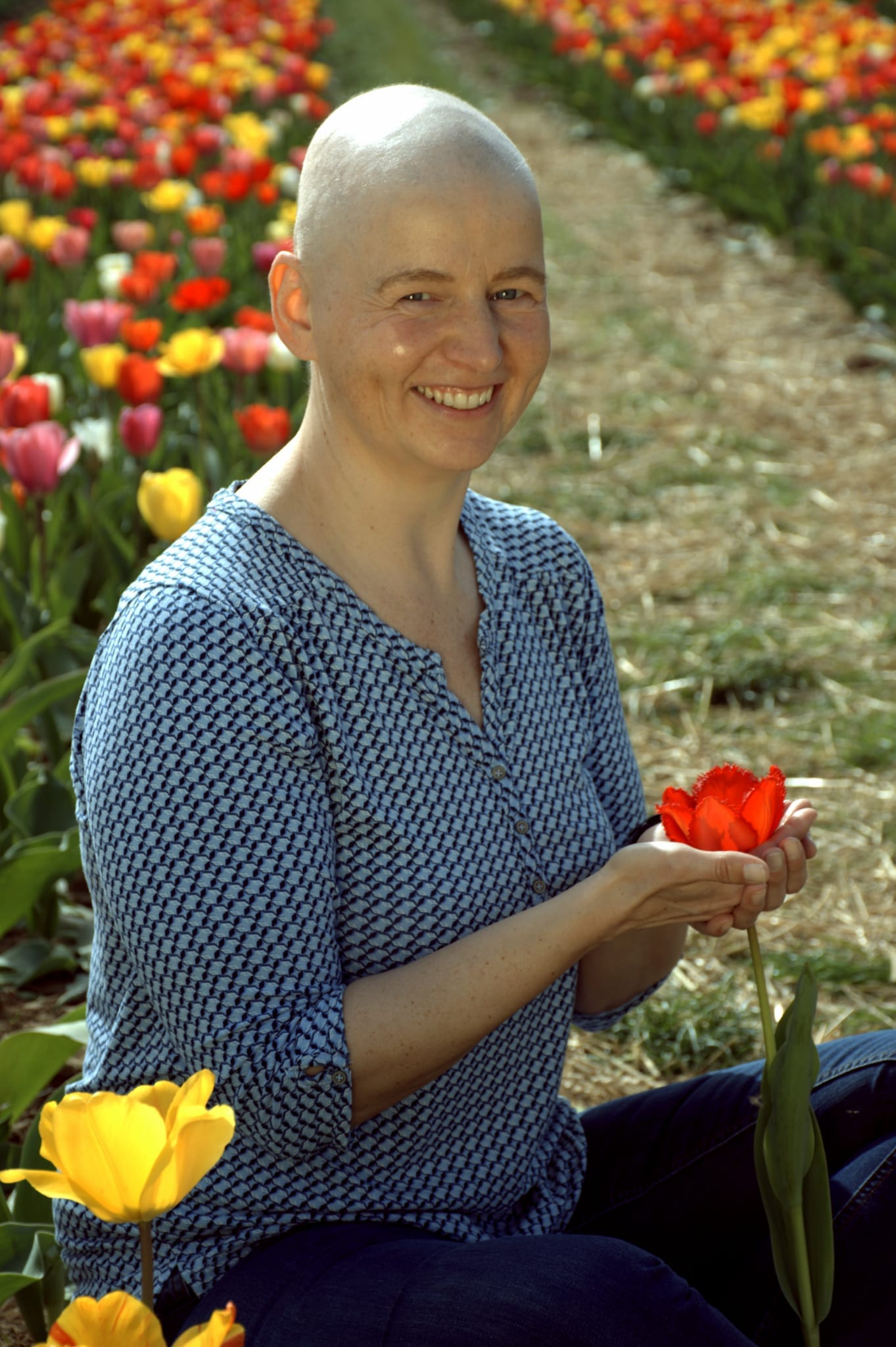 Danielle sitzt mit einer roten Tulpe in der Hand zwischen blühenden Tulpenreihen