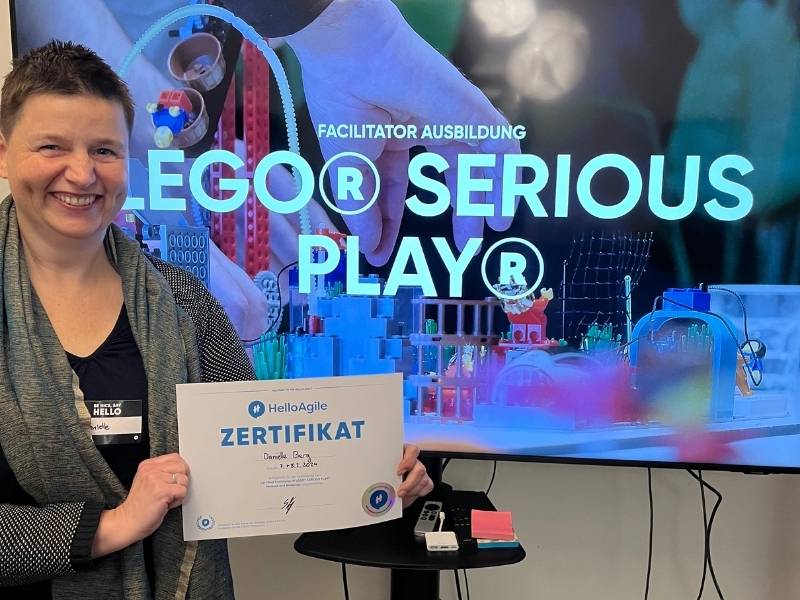 Danielle Berg - mit Lego® Serious Play® Facilitator Zertifikat vor einem großen Bildschirm mit Lego® Serious Play® Facilitator Präsentation