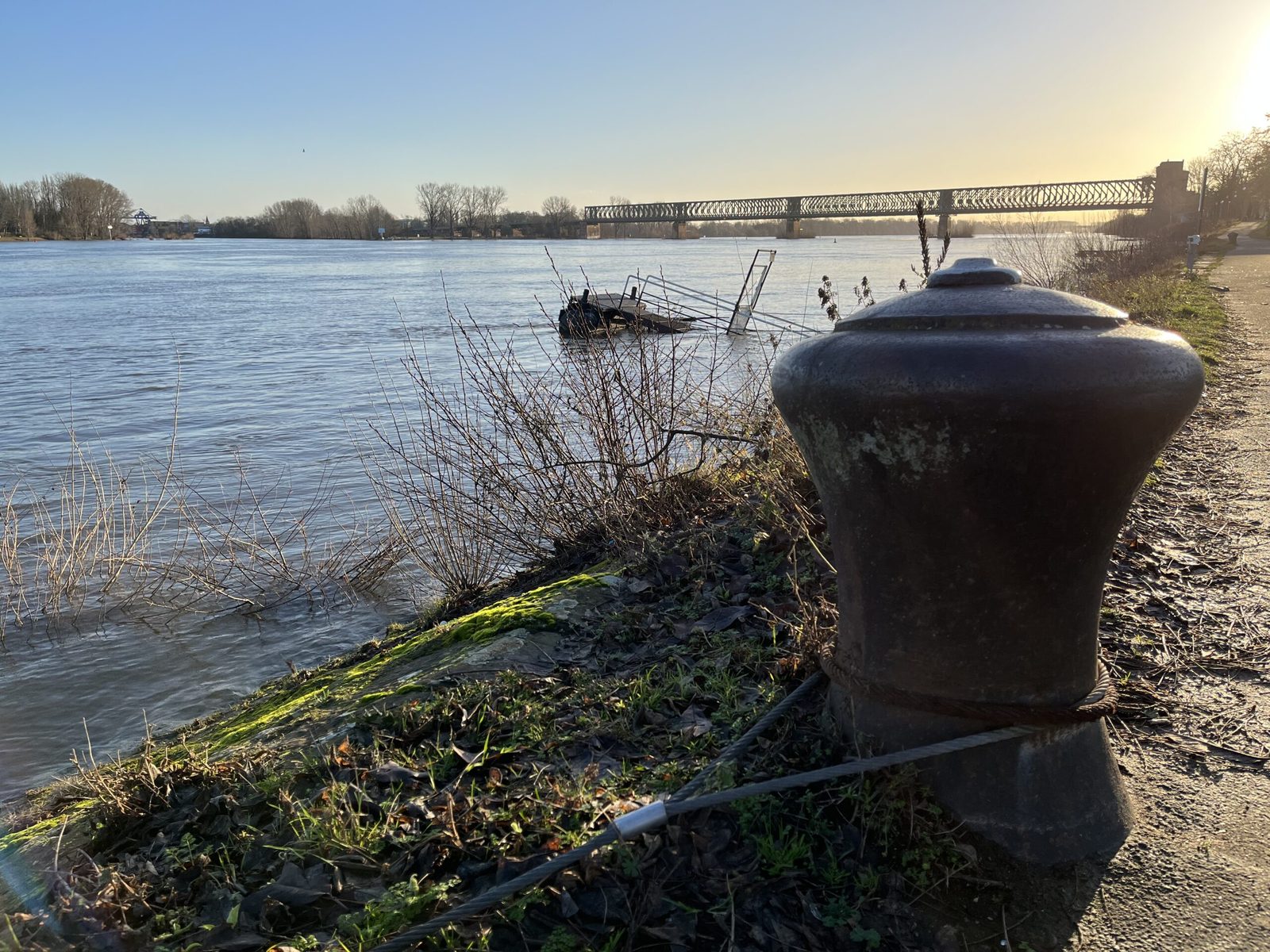 Poller am Rheinufer, dahinter Anleger und Eisenbahnbrücke