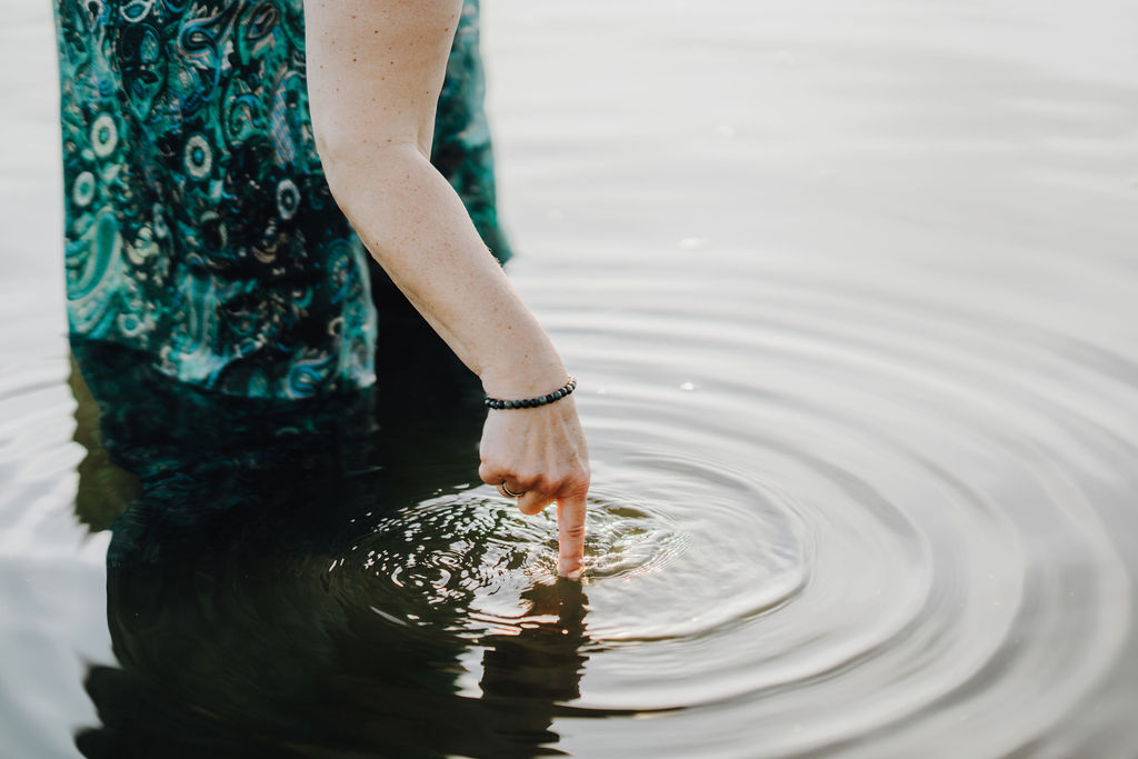 Eine Hand berührt die Wasseroberfläche, die Wellen ziehen ihre Kreise