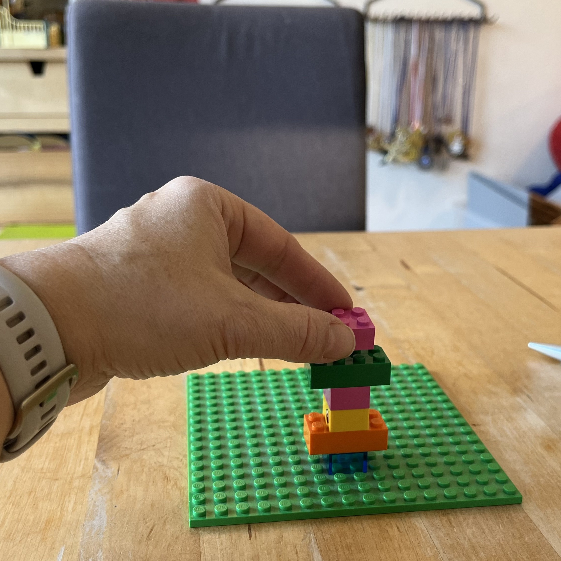 Hand setzt einen rosa LEGO Stein auf ein kleines Modell auf einer grünen 16x16 Grundplatte