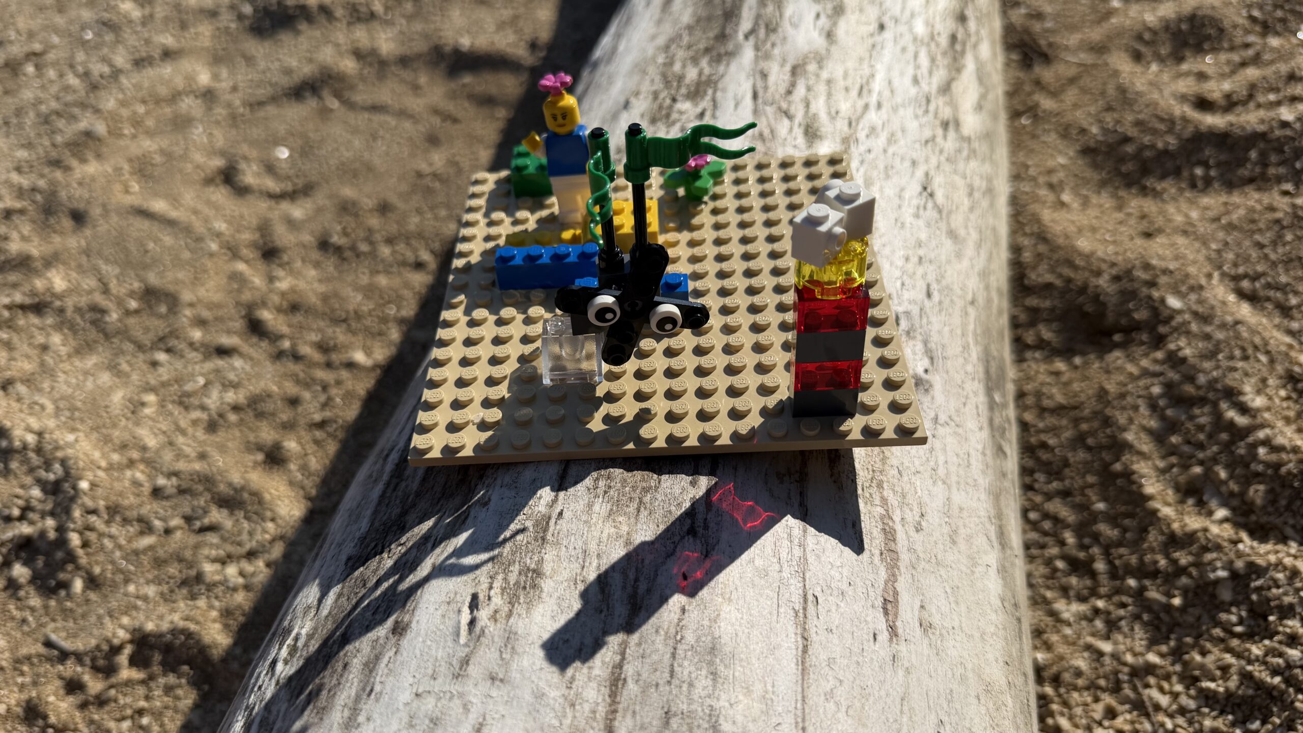 Kleines LEGO Modell auf einer 16x16 Grundplatte, draußen auf einem Baumstamm in der Sonne