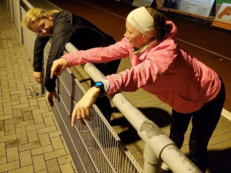 zwei müde Läuferinnen hängen mit dem Oberkörper am Stadionzaun