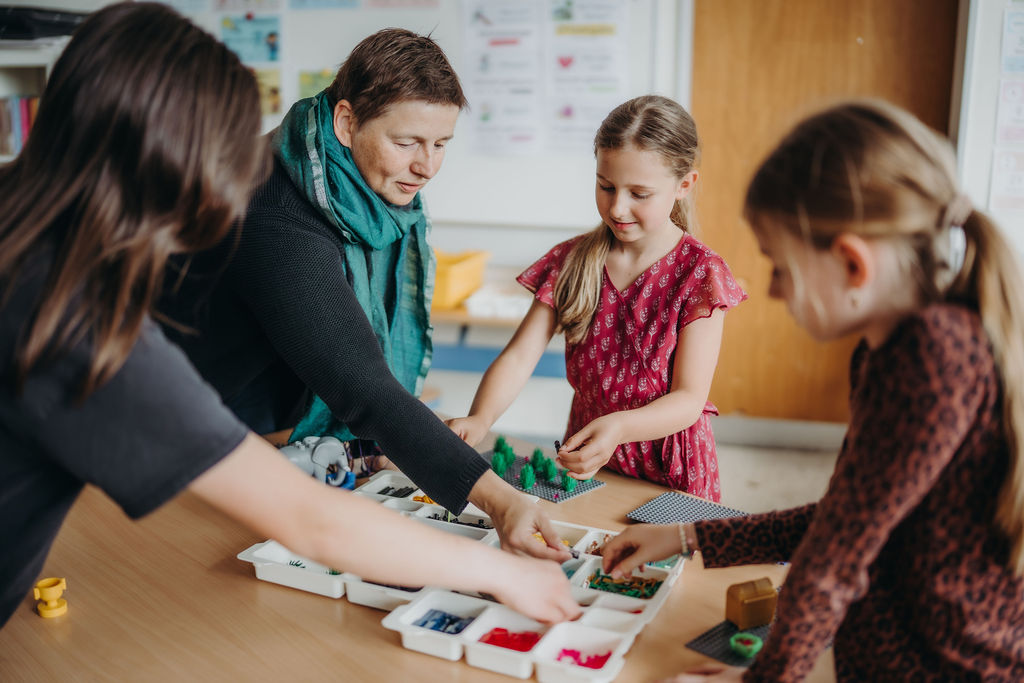Danielle Berg baut mit drei Mädchen an einem Tisch voller LEGO® Steine im Klassenzimmer
