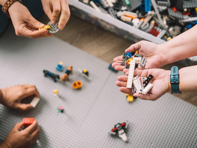 Zwei Hände halten LEGO Steine über einem gemeinsam gebauten Modell im Workshop